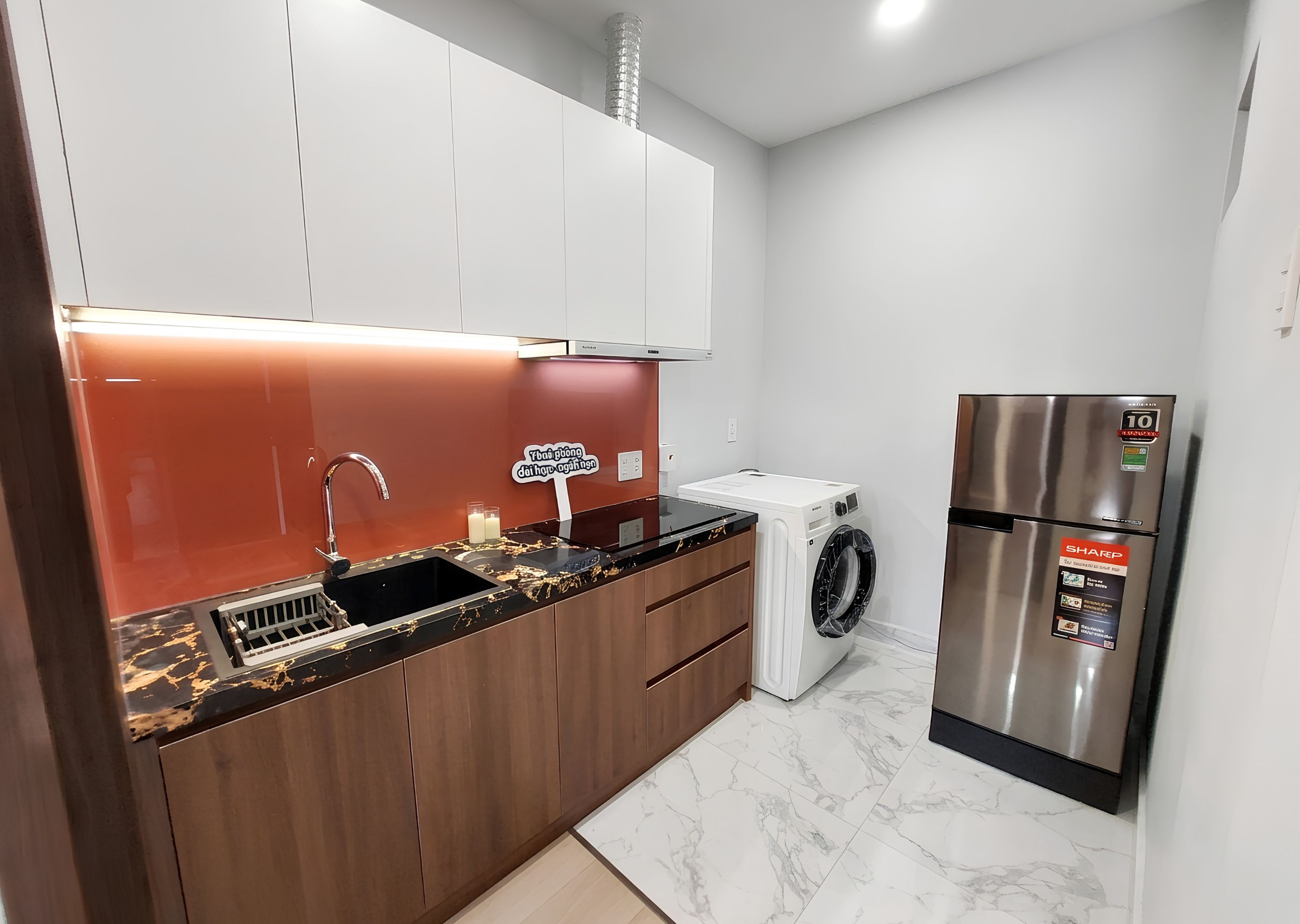 A modern kitchen with a stainless steel refrigerator, a built-in washing machine, and a marble-tiled floor.