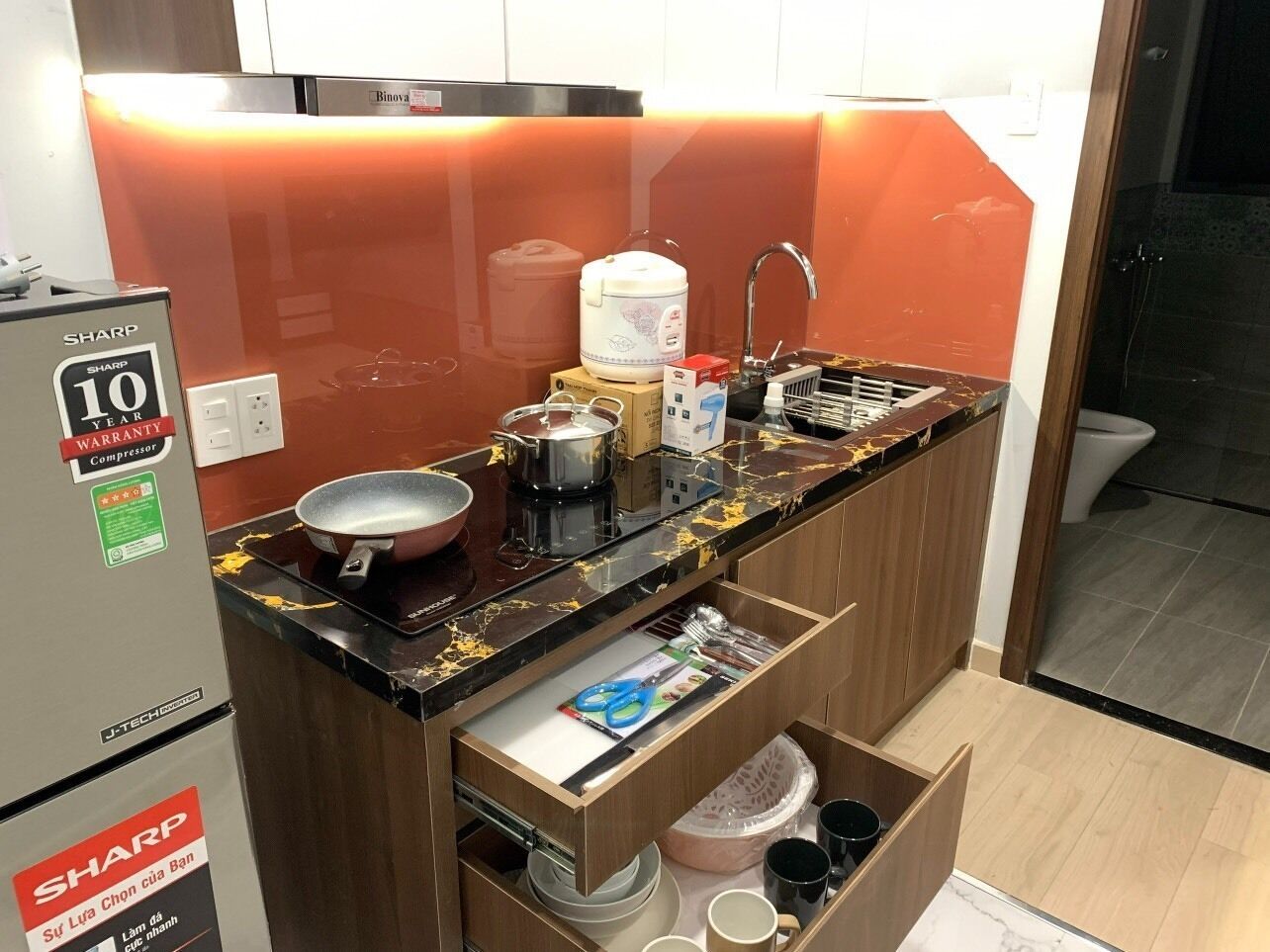 A compact kitchen with a Sharp refrigerator, a sink, and a countertop with various kitchen items.