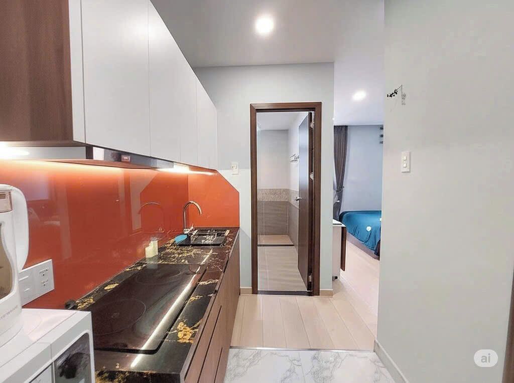 A compact kitchen with a modern stove, a microwave, and a sink. There is a doorway leading to a bathroom with a shower and a toilet.