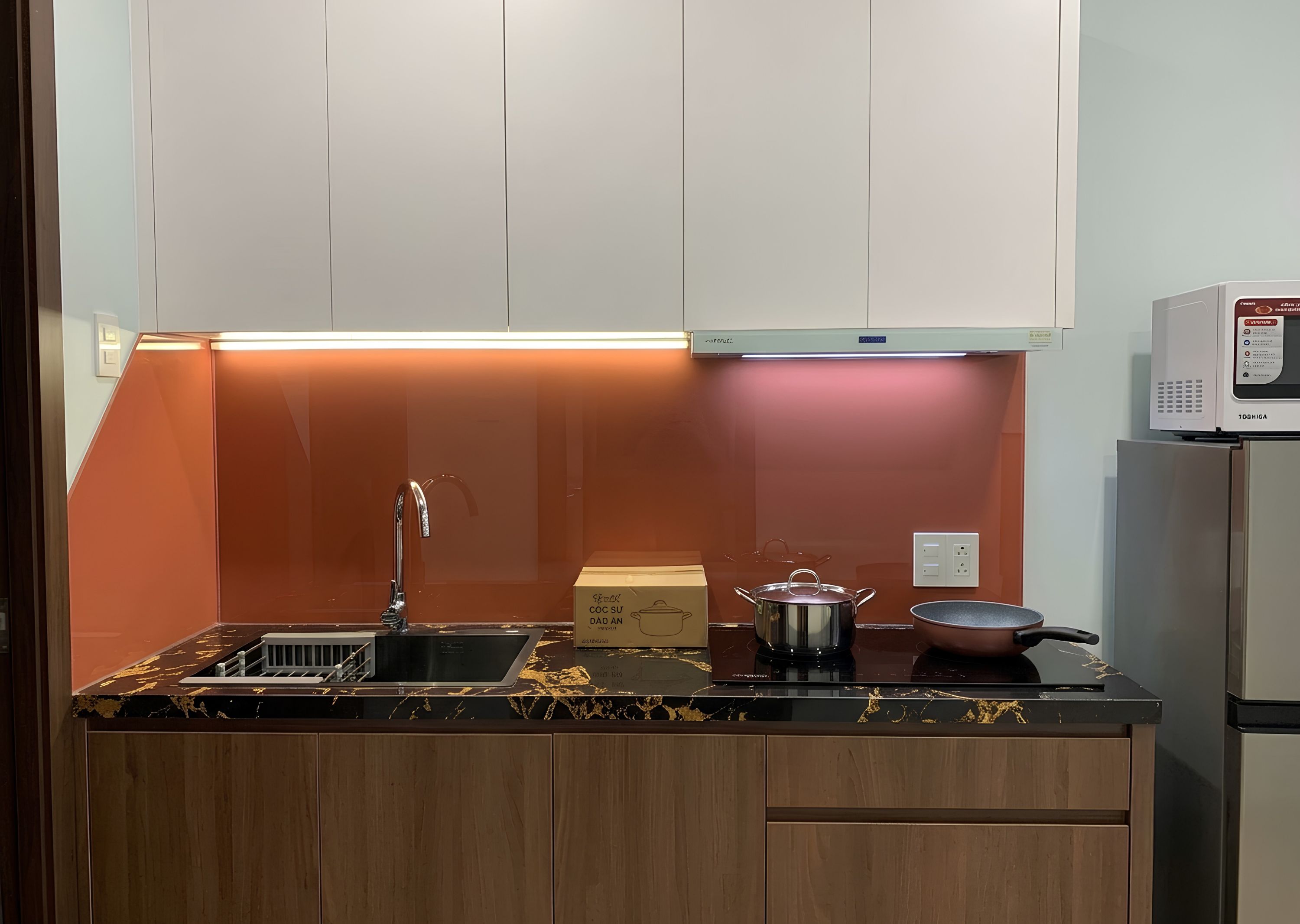 Een kleine keuken met een spoelbak, aanrecht, keukenkastjes, een magnetron en een pan.