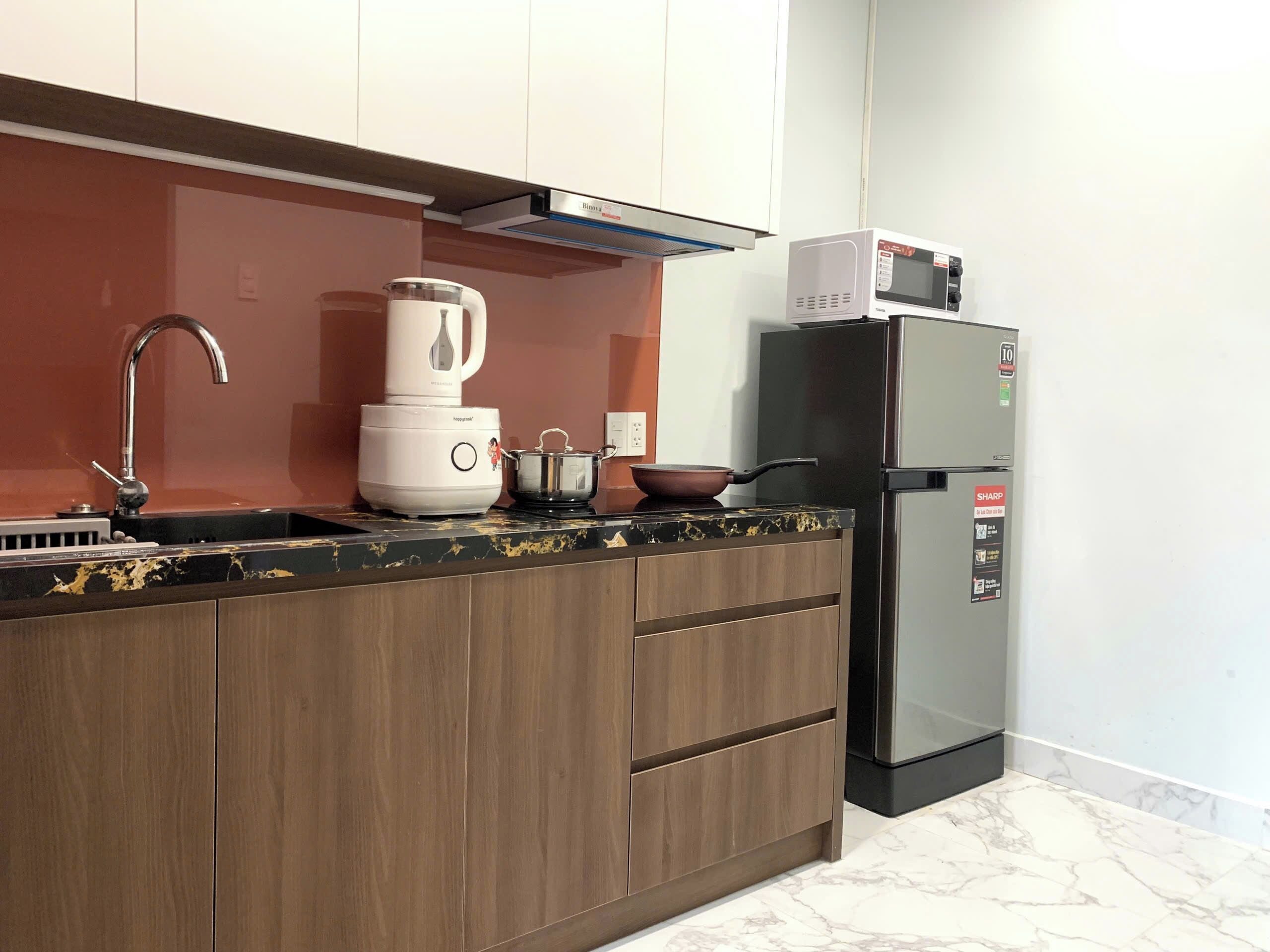A modern kitchen with a built-in stove, a blender, a refrigerator, and wooden cabinets.