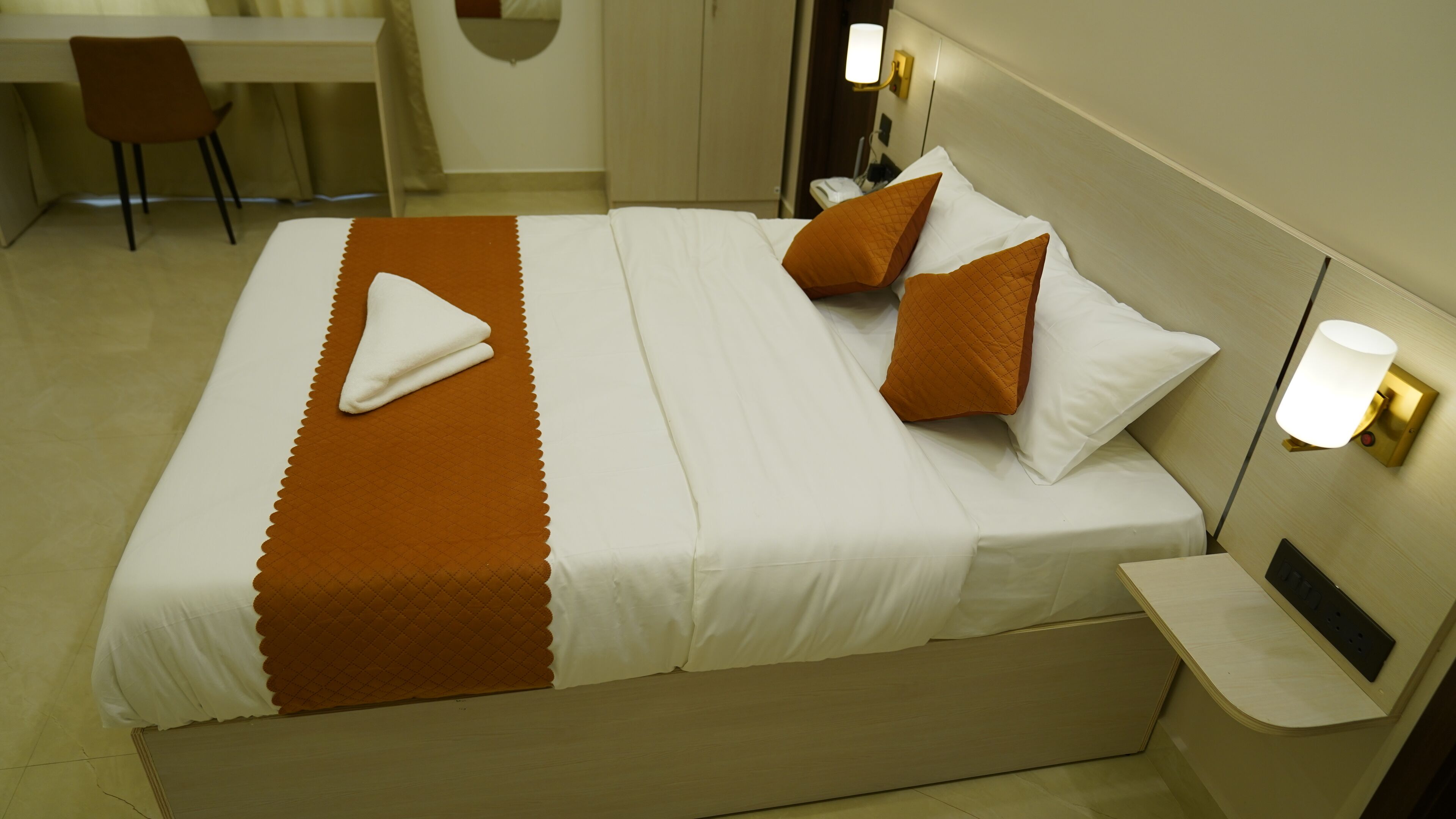 Una camera d'albergo con un letto, un comodino, una lampada, una sedia e una scrivania.