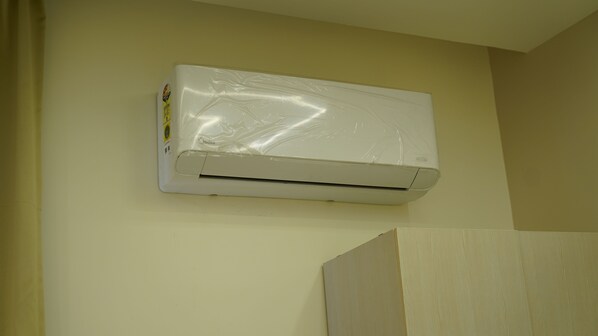 A white air conditioning unit mounted on a wall with a beige wall and a wooden panel below. - Ustay (Hyderabad)