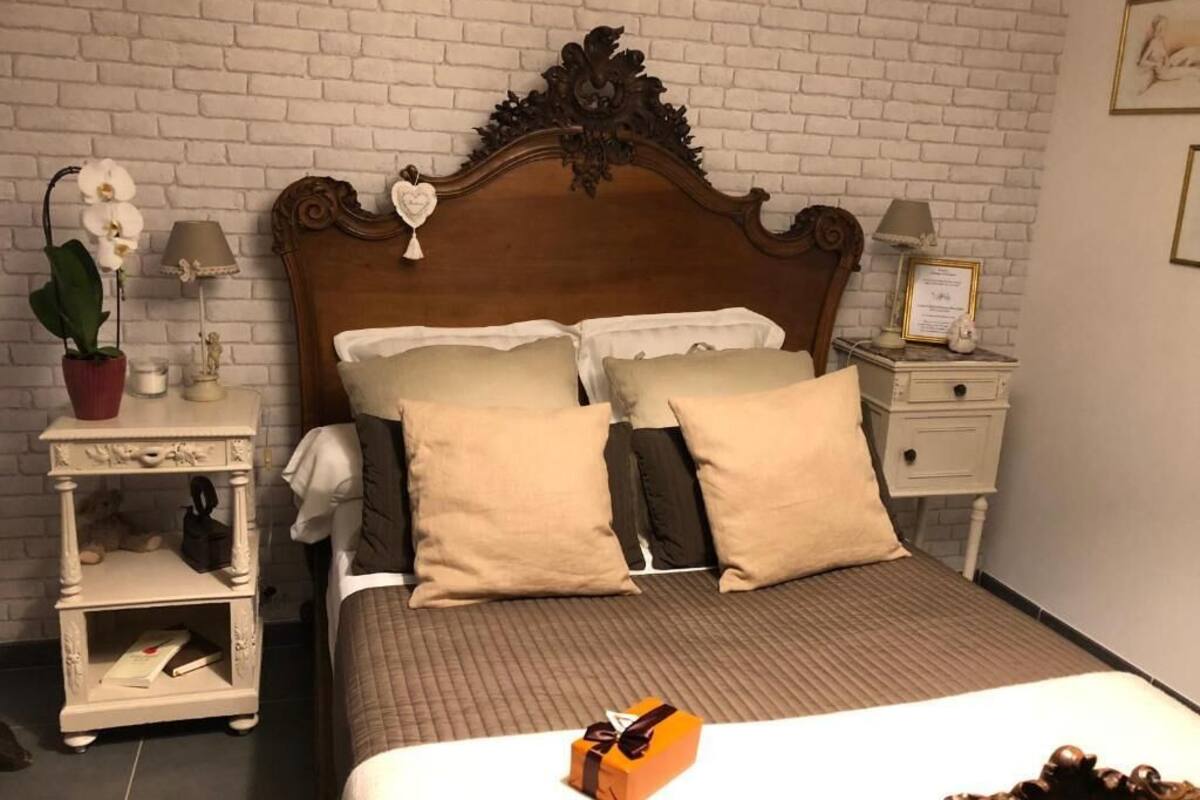 Une chambre à coucher avec une tête de lit en bois, deux tables de chevet, une petite table de nuit, une plante en pot et un certificat encadré accroché au mur.