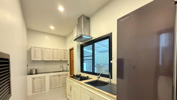 A modern kitchen with white cabinets, a stainless steel range hood, a black sink, and a large window. - Baan Wang Tan 1 Luxury Pool Villa, Chiang Mai (Chiang Mai)