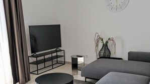 A modern living room with a flat-screen TV, grey sofas, a black coffee table, and a decorative vase. - Munich Finest Apartments 16 by Interhome (Munich)