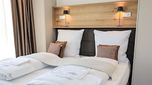 A neatly made bed with white linens and pillows, a wooden headboard with two wall-mounted lamps, and a window with curtains. - Munich Finest Apartments 20 by Interhome (Munich)