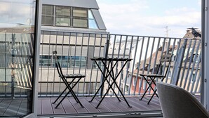 A balcony with a table and chairs, a view of a modern building, and a pigeon on the railing. - Munich Finest Apartments 20 by Interhome (Munich)