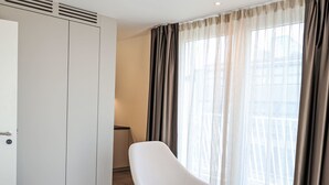 A modern hotel room with a large wardrobe, a comfortable chair, and a view of the city through sheer curtains. - Munich Finest Apartments 20 by Interhome (Munich)