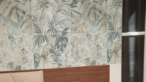 A hotel room with a wooden headboard, a potted plant, a bedside phone, and a wall with tropical wallpaper. - Hotel Rajputana International Raipur (Raipur)