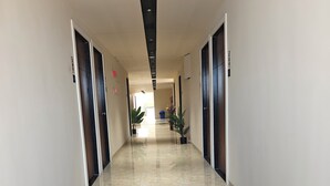 A long, narrow hallway with a polished marble floor, flanked by doors on both sides, leading to a bright room in the distance. - Hotel Gokul Inn (Vapi)
