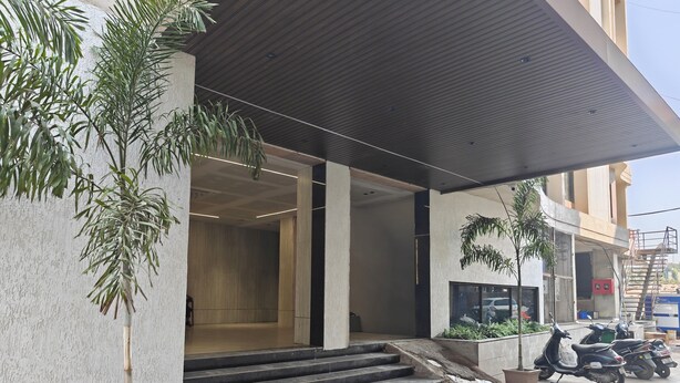 A modern building entrance with a concrete facade, a set of stairs leading to the entrance, and a few potted plants. - Hotel Gokul Inn (Vapi)