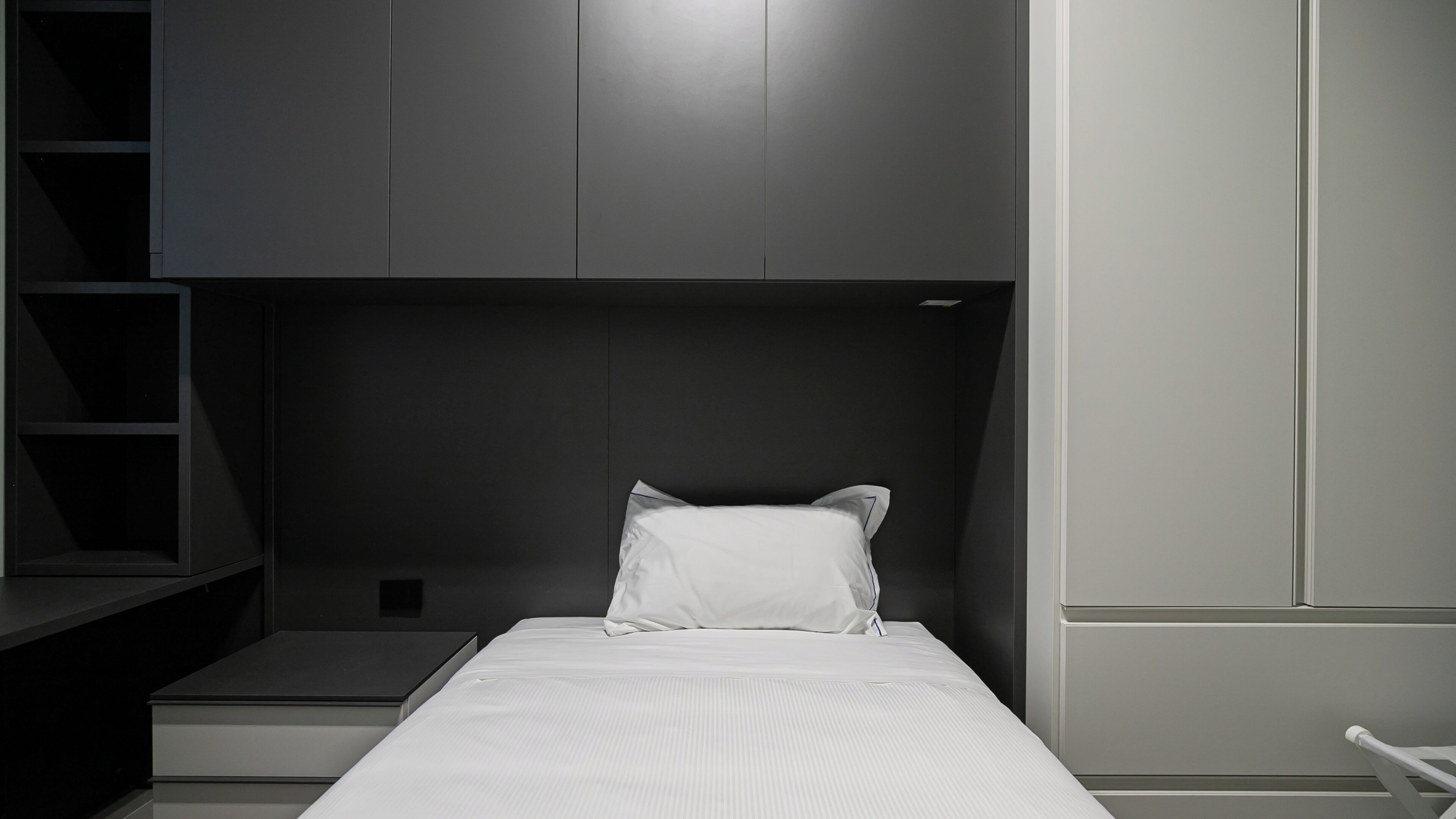 Un dormitorio moderno con cama, mesita de noche y estanterías empotradas.