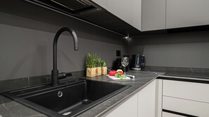 A modern kitchen with a black sink, stainless steel faucet, and a marble countertop. There are two brown paper bags labeled "HEAR'S GARDEN" on the counter. - Italianway Comfort - Monte Nevoso 8 (Milan)