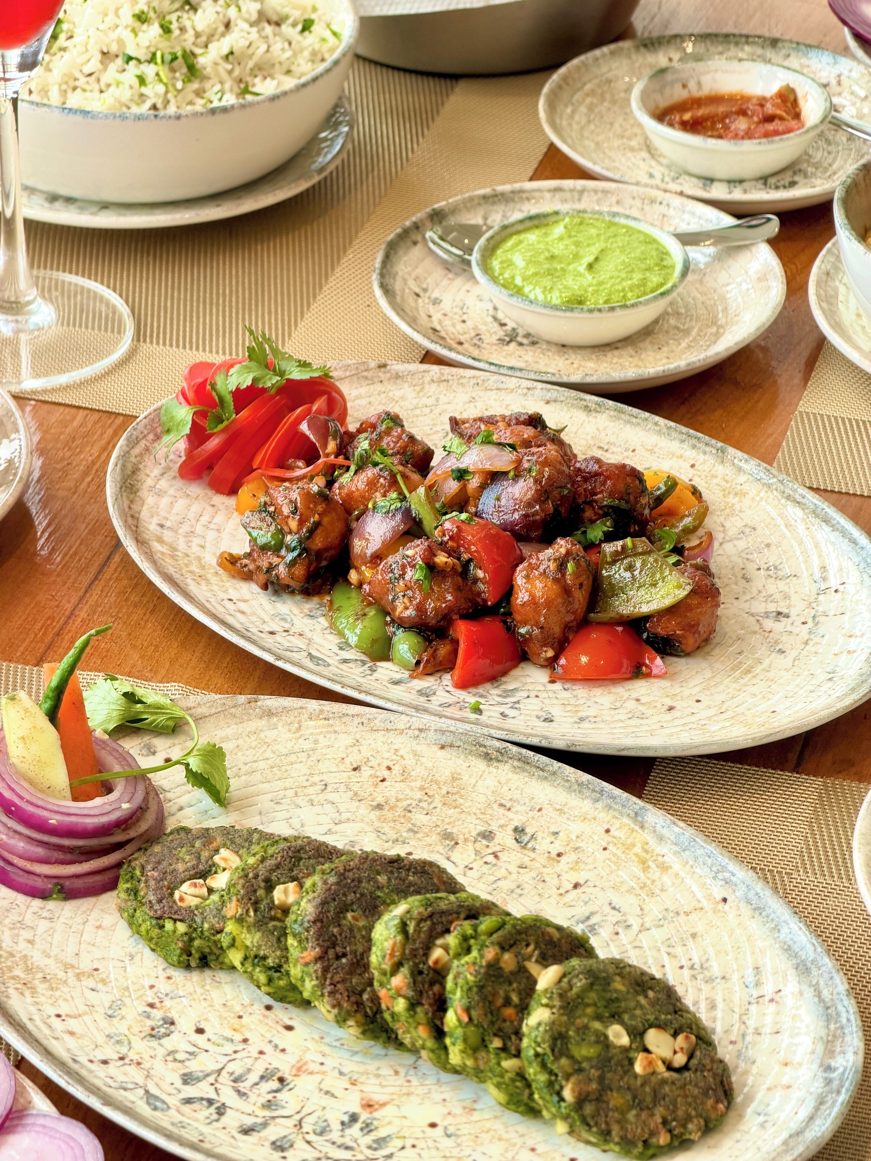 A table with various dishes, including grilled meat, vegetables, and a green sauce.