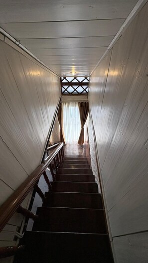 A wooden staircase with a handrail, leading to a room with a window and curtains. - Cochrane Place By Teesta Hotels (Kurseong)
