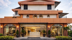 Un hotel moderno con una estructura de dos pisos, una entrada destacada con puertas de cristal y una terraza en la azotea.