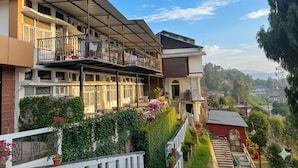 Un edificio de varios pisos con balcones, un área de estar exterior cubierta y vistas a un paisaje montañoso.
