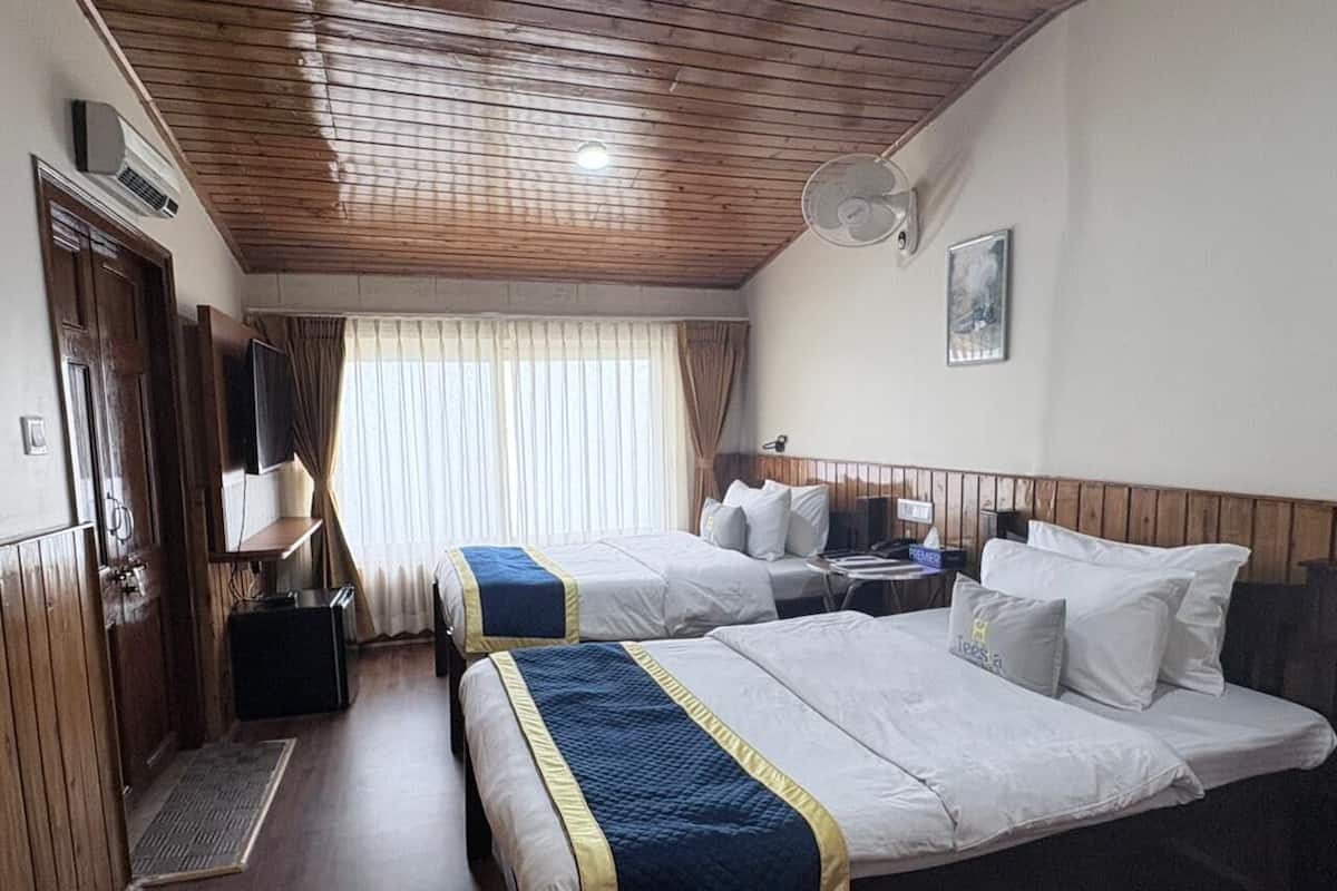 Ein Hotelzimmer mit zwei Betten, einem Schreibtisch, einem Sessel, einem Fernseher und einem Fenster mit Vorhängen.