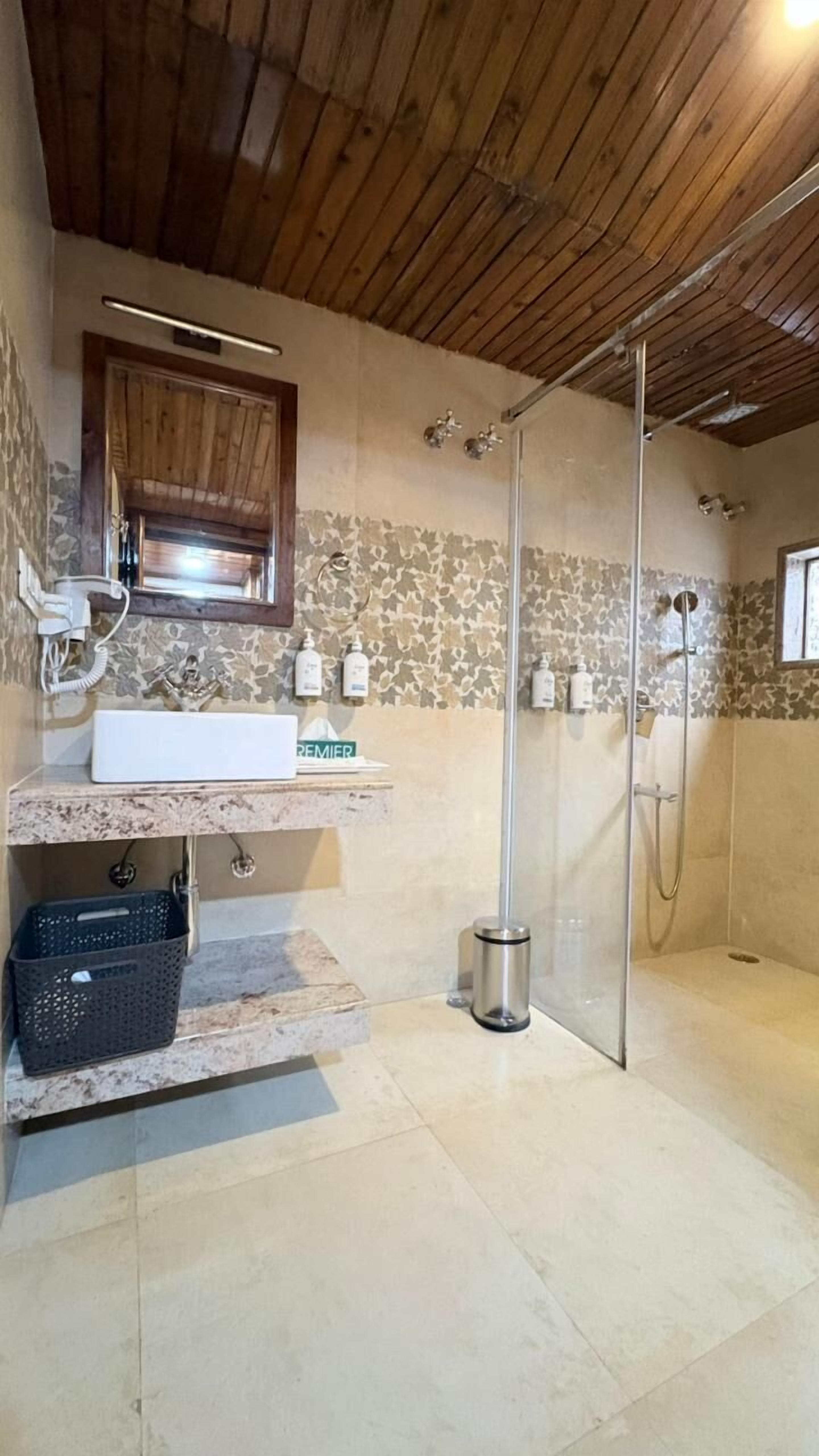 Een badkamer met een houten plafond, een wastafel met een marmeren aanrechtblad, een douche met een glazen deur en een behang met patroon.