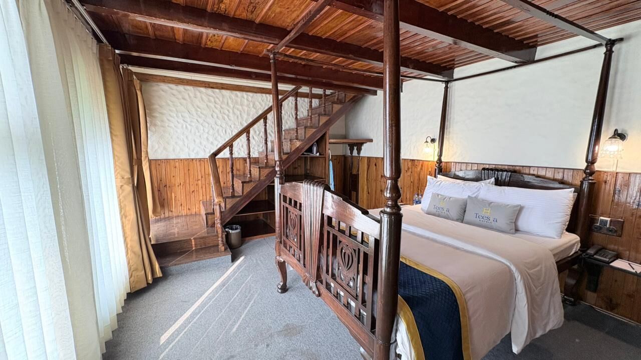 Ein Bett mit Baldachin, ein Holzkopfteil, eine Holztreppe und Blick auf eine strukturierte Wand.
