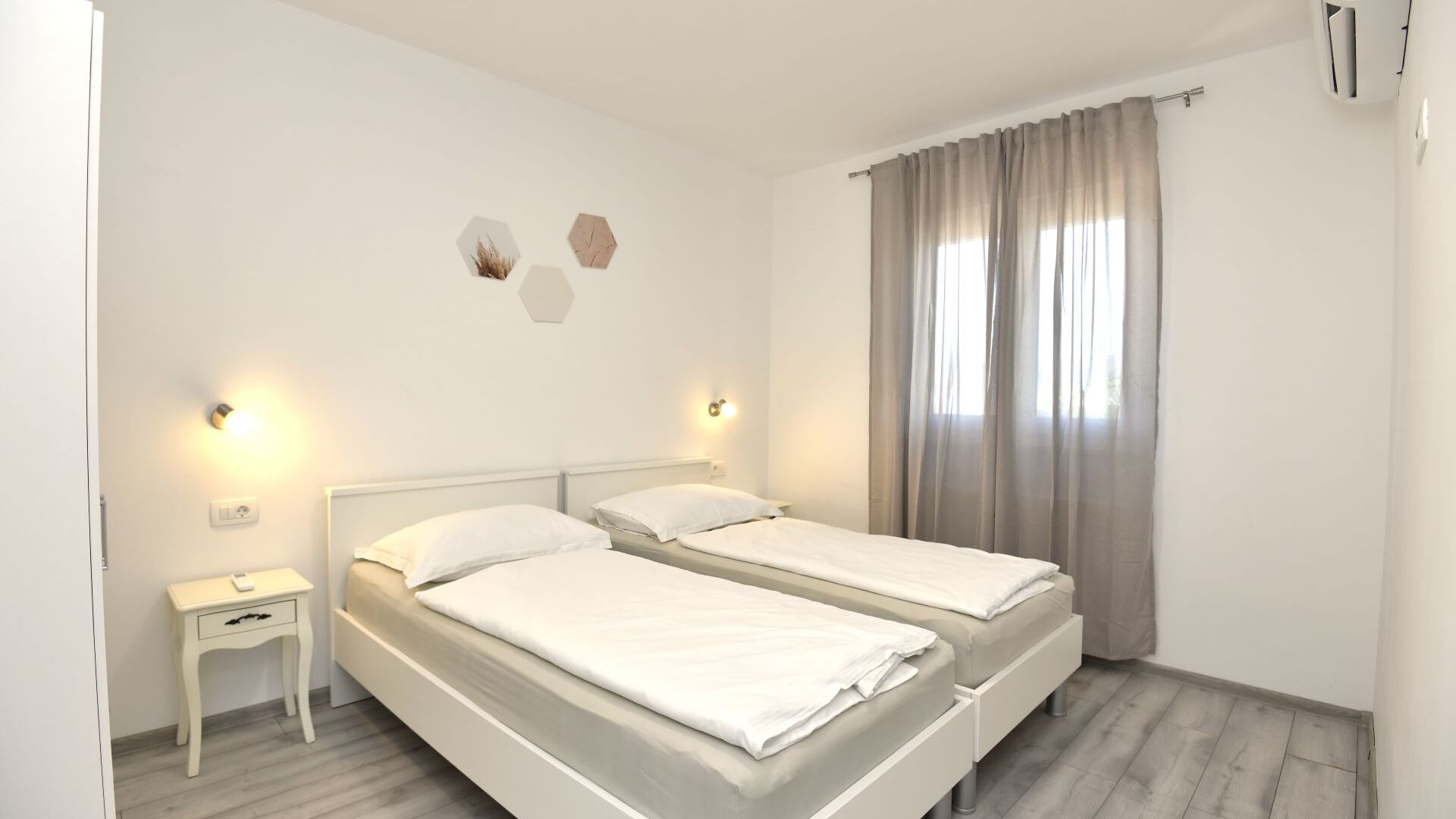 Ein Schlafzimmer mit zwei Betten, Nachttischen, Wandleuchten und einem Fenster mit Vorhängen.