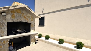 An outdoor grill area with stone walls, a small window, and a paved walkway with bushes. - Villa Marica-Grubine by Villas Guide (Grubine)