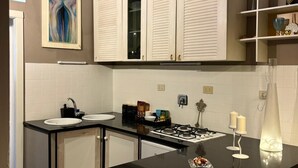 Una cucina moderna con mobili bianchi, un piano di lavoro nero e un fornello a gas. Una lavandino a sinistra e un vaso decorativo a destra.