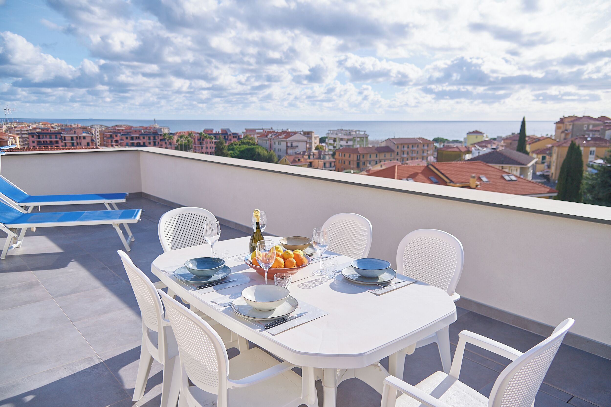 Eine Dachterrasse mit Esstisch, Stühlen und Blick auf Stadt und Meer.