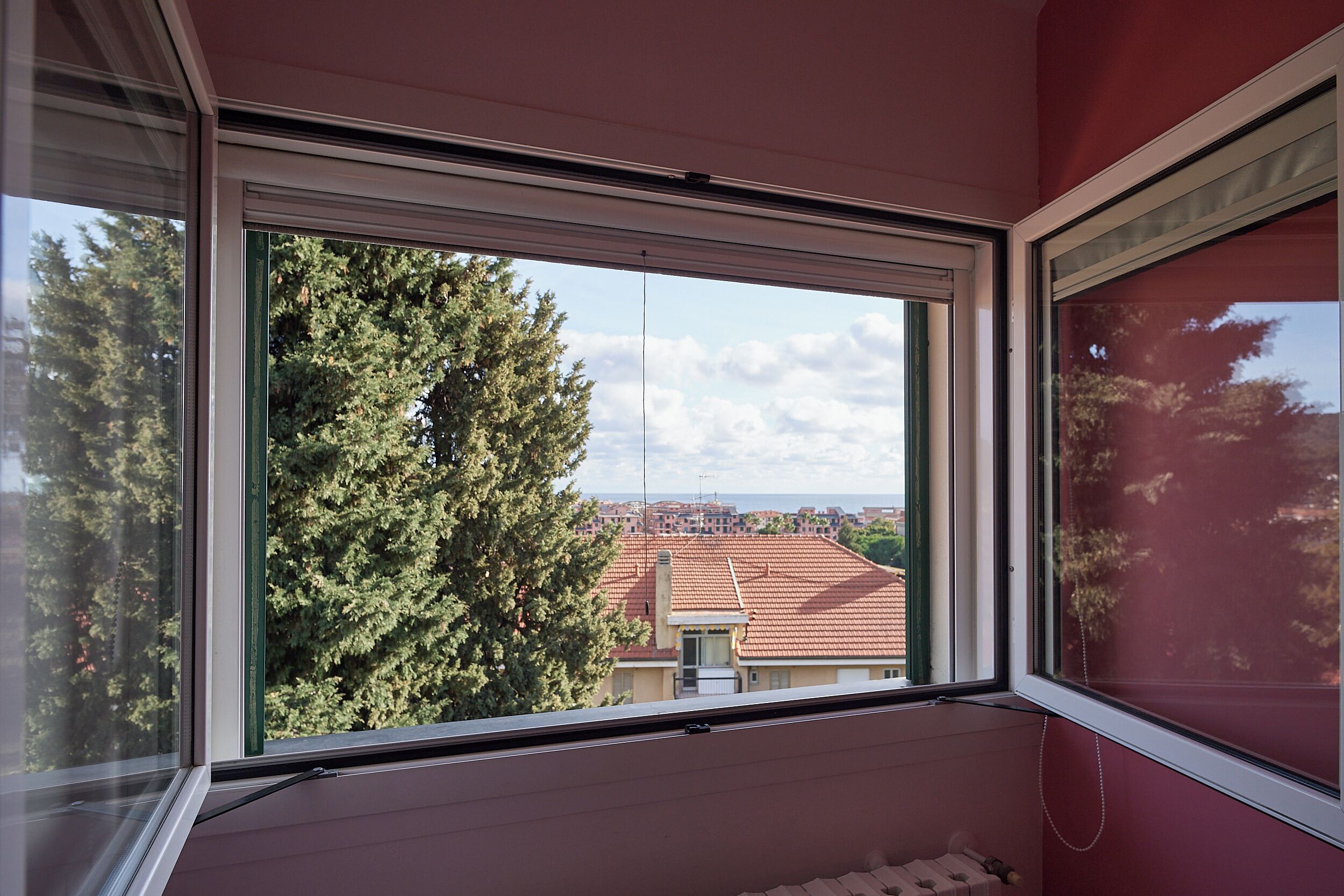 A room with a large window overlooking a red-tiled roof and a tree.