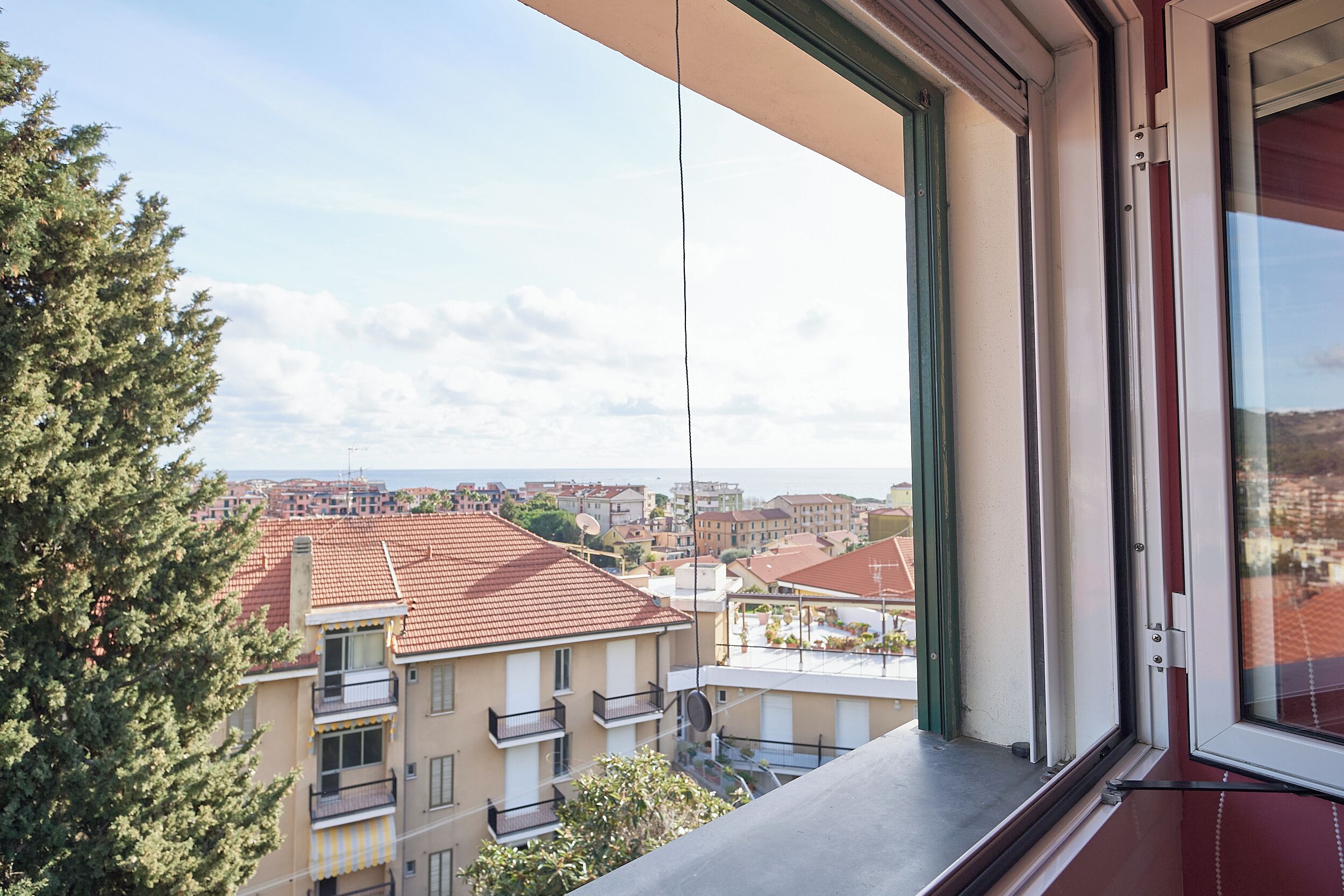 Un balcón con vista a un paisaje urbano, incluyendo edificios con tejados rojos y un cielo despejado.