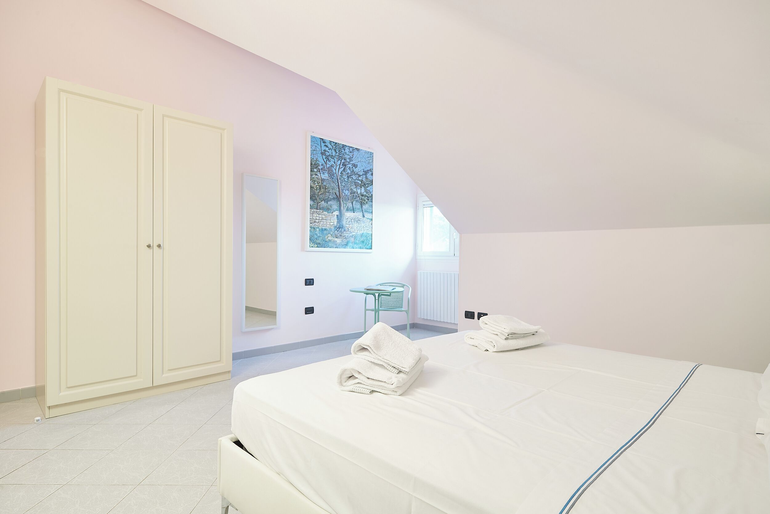 A bedroom with a bed, a chair, a painting, and a wardrobe.