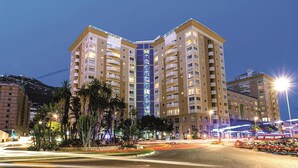 Un hotel de varios pisos con balcones, un atrio central y una zona ajardinada con palmeras.