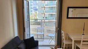 Un salón con sofá, una mesa y un balcón con vistas a edificios.