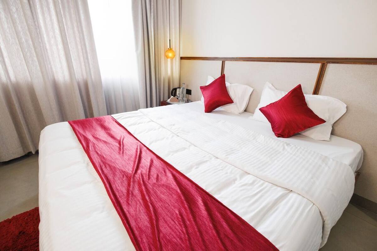 A hotel room with a large bed, white bedding, and red accents.