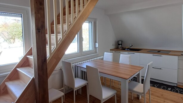Une cuisine moderne avec des meubles blancs, une table à manger en bois et un escalier en bois.