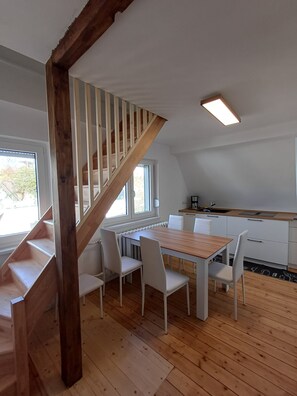 Una cocina moderna con armarios blancos, una mesa de comedor de madera y una escalera de madera.