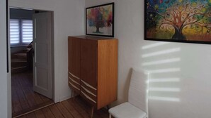 Un couloir avec un plancher en bois, une chaise blanche, un meuble en bois et un luminaire au plafond.