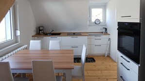 Une cuisine moderne avec des meubles blancs, une table à manger en bois et un four encastré.