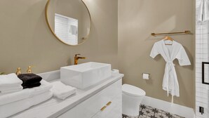 Une salle de bain moderne avec un grand miroir, des robinets dorés, un lavabo blanc et des toilettes.