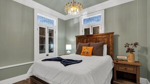 Une chambre à coucher avec un grand lit, une table de chevet en bois, un lustre et une fenêtre donnant sur un beau paysage.