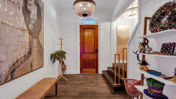 Un couloir avec un banc en bois, une grande peinture abstraite, une porte en bois et un escalier avec une chaise rouge.