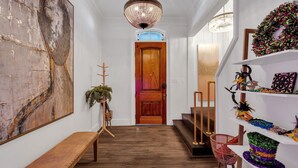 Ein Flur mit einer Holzbank, einem großen abstrakten Gemälde, einer Holztür und einer Treppe mit einem roten Stuhl.