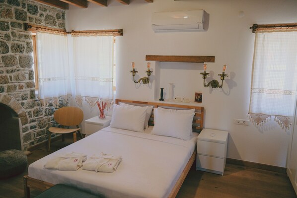 A bedroom with a stone wall, a wooden bed frame, a bedside table, a nightstand, and a chair. - Madran (Datca)