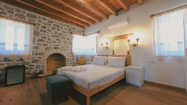 Ein Schlafzimmer mit Steinwand, Holzbalken, einem Bett, Nachttischen und einem Kamin.