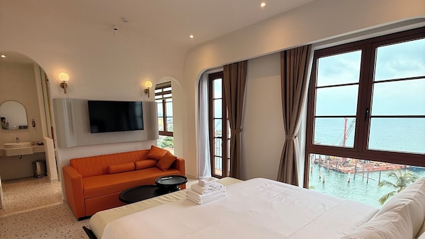Une chambre d’hôtel moderne dotée d’un grand lit, d’un canapé, d’une télévision et offrant une vue sur la mer.