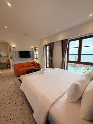 Un hotel moderno con una cama grande, un sofá, un televisor y vista al mar.