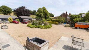 A gravel parking area with a fire pit, a red car, and an orange van. - Tranquil Cottage in a Countryside (Ashford)