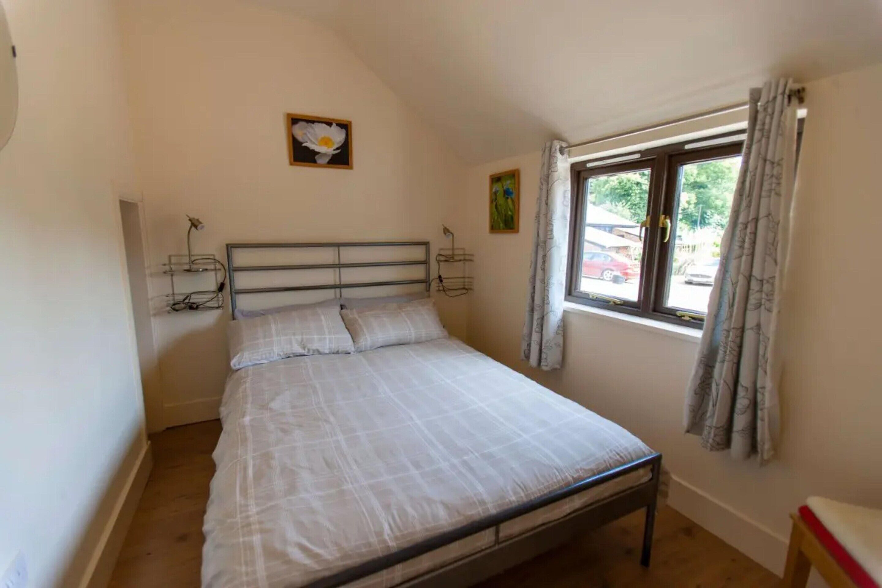 A small, single-bed room with a metal headboard, a bedside table, and a window with curtains.
