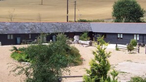 A rustic building with a sloped roof, surrounded by a gravel driveway and sparse vegetation. - Tranquil Cottage in a Countryside (Ashford)